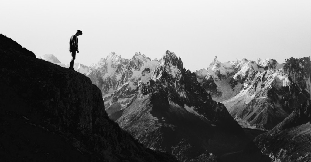 Man standing at the edge of a steep cliff and looking down as if ready to jump