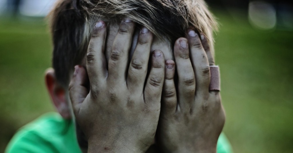 A sad, small boy has covered his face with his hands