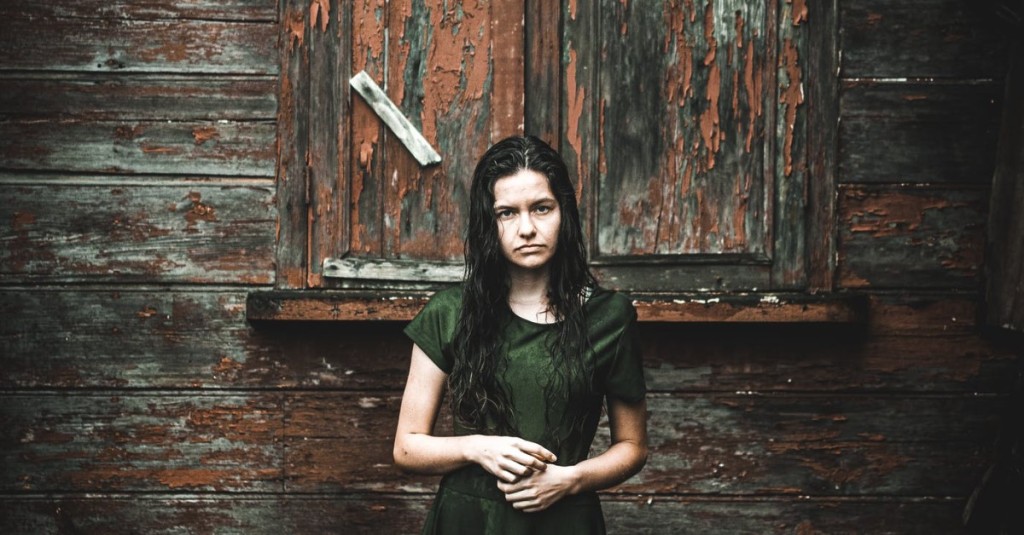 A troubled and sad woman standing in front a rundown building face