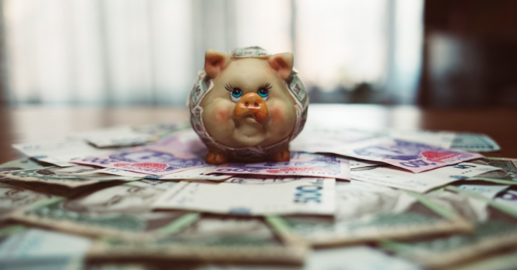 A porcelain piggy standing on currency and wrapped in currency notes