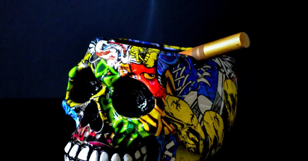A multicolored skull ashtray with a lit cigarette placed inside it
