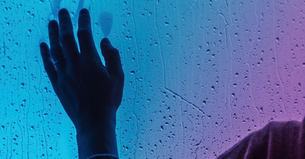 A hand pressed against a window with water droplets on it