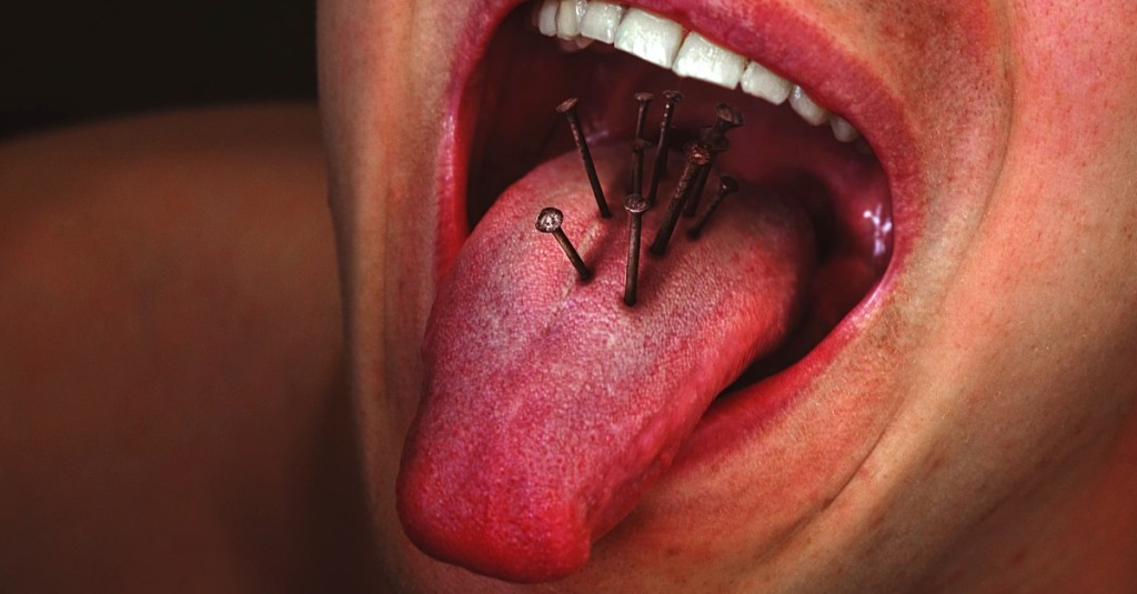 A close up of a man sticking out his tongue and there are nails embedded in it