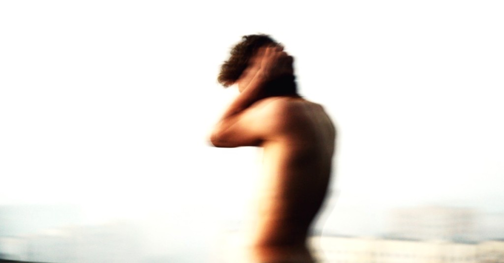 The side blurry profile of a bare chested man covering his ears with the palms of his hands