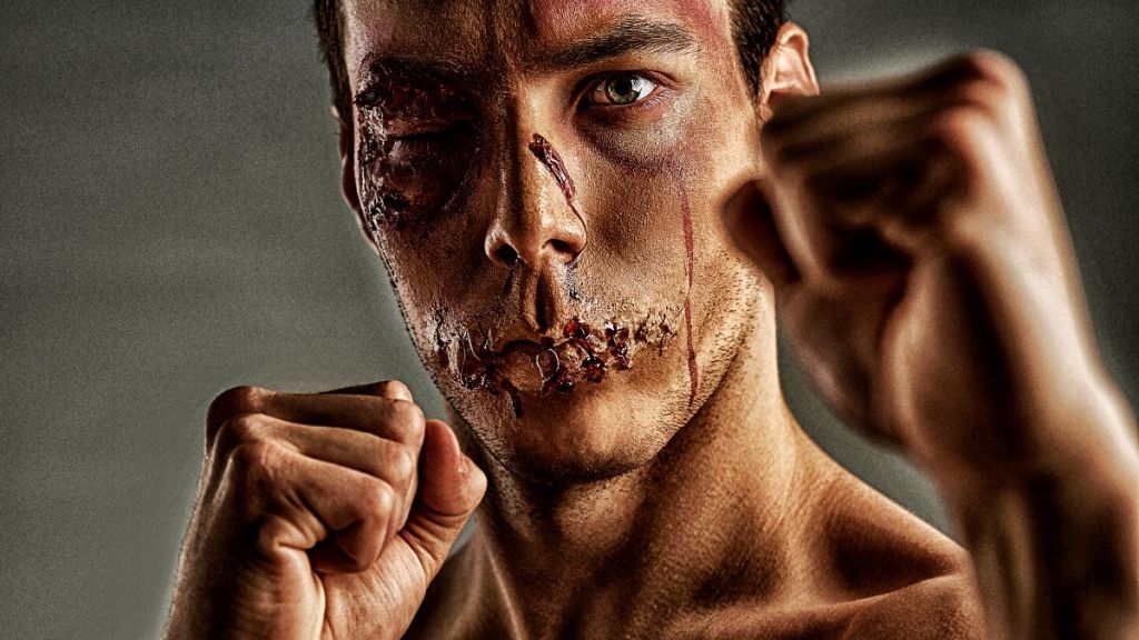 A young man with a bloody beaten up face and his fists raised at face level