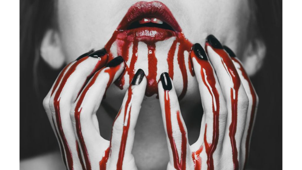 The close up of a woman's lower face with bloody lips and blood dripping down her chin and her bloody fingers upon her chin
